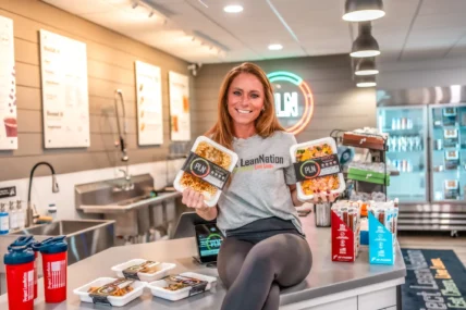 A woman holding Project LeanNation meals in a kitchen.