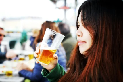 A young woman drinking a beer in a glass.