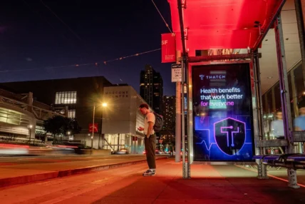 A man standing outside at night near a Thatch billboard.